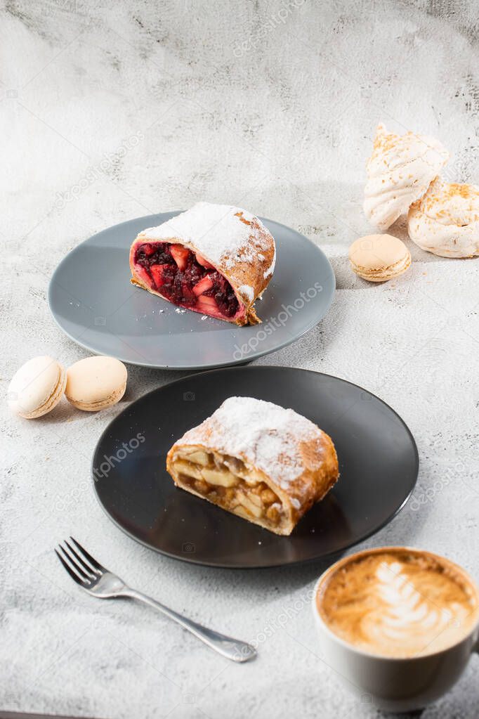 Homemade Traditional Austrian apple strudel with fresh apples, nuts and powdered sugar. Menu for cafe. Piece of cake on black plate, white cup on white marble background. Vertical photo.