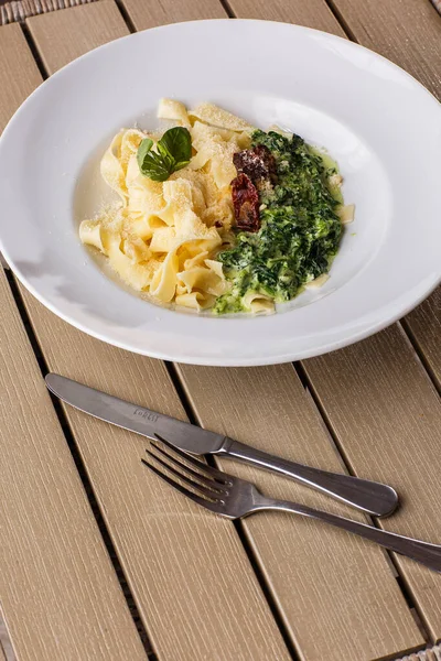 Tagliatelle vegetarian Pasta Dish with spinach and dried tomatoes decorated with basil. Delicious lunch with pasta and spinach. On wooden background.