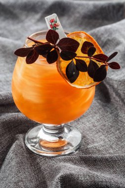 Parlak turuncu, gri arkaplanlı viski kokteyli. Kuru portakal dilimi ve bitkiyle süslenmiş. Mükemmel Hizmet örneği. Dikey. Alkol kartı. Bar menüsü