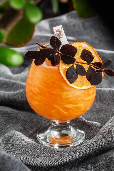 Bright orange Old Fashioned Cocktail with whiskey on a gray background. Decorated with dry orange slice and herb. Perfect Serve example. Vertical. Alcohol card. Bar menu