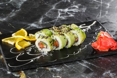 Somon, salatalık ve avokadoyla birlikte yeşil ejderha suşisi. Japon yemeği. Geleneksel Asya pirinç suşisi sağlıklı deniz ürünleri. Siyah mermer arka plan. Yatay fotoğraf.