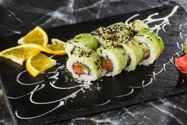 Somon, salatalık ve avokadoyla birlikte yeşil ejderha suşisi. Japon yemeği. Geleneksel Asya pirinç suşisi sağlıklı deniz ürünleri. Siyah mermer arka plan. Yatay fotoğraf.