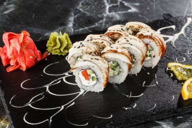 İçinde salatalık, domates, yılan balığı ve krem peynir olan suşi ruloları siyah mermer arka planda izole edilmiş. Philadelphia unagi rulosu. Suşi menüsü. Yatay fotoğraf.