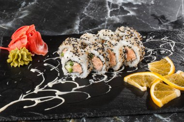 Siyah mermer arka planda izole edilmiş siyah tahtada ton balığı, somon, salatalık ve krem peynirli suşi ruloları. Kaliforniya dürümleri siyah tobiko ya da masago havyarı ile kaplıdır. Suşi menüsü. Yatay fotoğraf