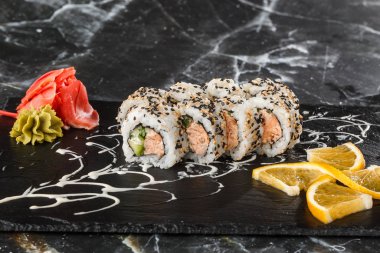 Siyah mermer arka planda izole edilmiş siyah tahtada ton balığı, somon, salatalık ve krem peynirli suşi ruloları. Kaliforniya dürümleri siyah tobiko ya da masago havyarı ile kaplıdır. Suşi menüsü. Yatay fotoğraf