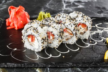 İçinde domates, yılan balığı, yengeç eti ve krem peynir olan suşi ruloları siyah mermer arka planda izole edilmiş. Kaliforniya dürümleri siyah tobiko ya da masago havyarı ile kaplıdır. Suşi menüsü. Yatay fotoğraf
