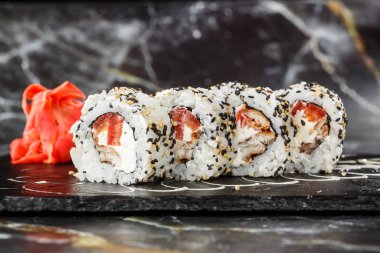 İçinde domates, yılan balığı, yengeç eti ve krem peynir olan suşi ruloları siyah mermer arka planda izole edilmiş. Kaliforniya dürümleri siyah tobiko ya da masago havyarı ile kaplıdır. Suşi menüsü. Yatay fotoğraf