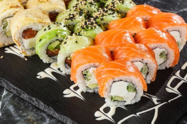 Siyah mermer arka planda servis edilen çeşitli suşiler. Japon yemeği için suşi menüsü. Japon suşi seti. Ton balığı, somon, karides, yengeç, havyar ve avokado. Yatay fotoğraf.