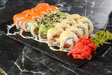 Siyah mermer arka planda servis edilen çeşitli suşiler. Japon yemeği için suşi menüsü. Japon suşi seti. Ton balığı, somon, karides, yengeç, havyar ve avokado. Yatay fotoğraf.