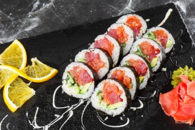 İçinde somon, avokado, ton balığı ve salatalık olan suşi ruloları. Maki Futomaki suşi rulosu ve siyah mermer arka planda somon balığı. Suşi menüsü. Japon yemeği. Yatay fotoğraf.