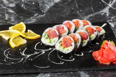 İçinde somon, avokado, ton balığı ve salatalık olan suşi ruloları. Maki Futomaki suşi rulosu ve siyah mermer arka planda somon balığı. Suşi menüsü. Japon yemeği. Yatay fotoğraf.