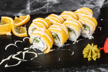İşlenmiş peynirli suşi ruloları, çedar, Amerikan peyniri, avokado, mango ve krem peyniri siyah mermer arka planda izole edilmiş siyah tahtada. Mangolu Philadelphia suşisi. Suşi menüsü. 