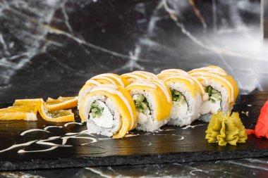 İşlenmiş peynirli suşi ruloları, çedar, Amerikan peyniri, avokado, mango ve krem peyniri siyah mermer arka planda izole edilmiş siyah tahtada. Mangolu Philadelphia suşisi. Suşi menüsü. 