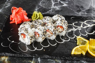 İçinde domates, yılan balığı, yengeç eti ve krem peynir olan suşi ruloları siyah mermer arka planda izole edilmiş. Kaliforniya dürümleri siyah tobiko ya da masago havyarı ile kaplıdır. Suşi menüsü. Yatay fotoğraf
