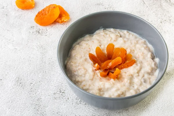 Oatmeal porridge or porridge oats or breakfast cereals with dried apricots isolated on white marble background. Homemade food. Tasty breakfast. Selective focus. Horizontal photo.