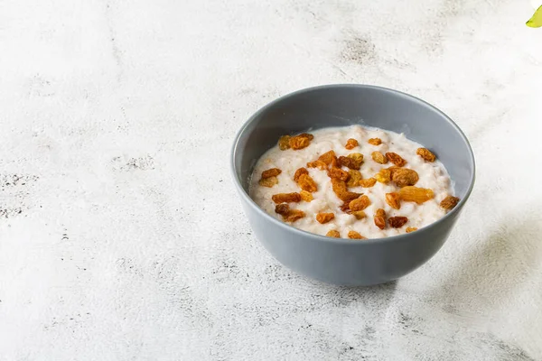 Oatmeal porridge or porridge oats or breakfast cereals with raisins isolated on white marble background. Homemade food. Tasty breakfast. Selective focus. Horizontal photo.