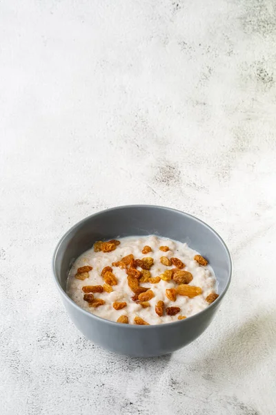 Oatmeal porridge or porridge oats or breakfast cereals with raisins isolated on white marble background. Homemade food. Tasty breakfast. Selective focus. Vertical photo.