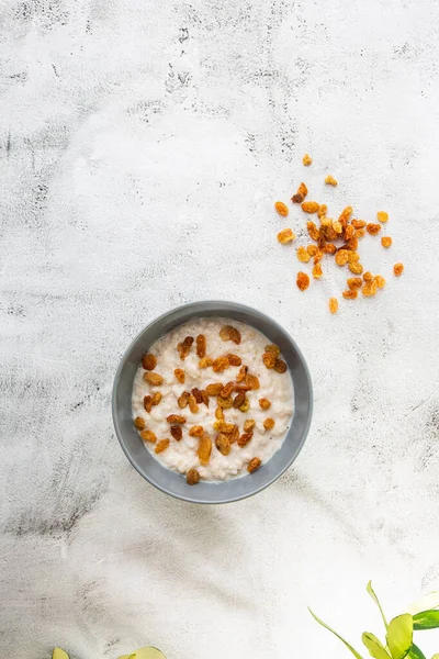 Avena gachas o gachas de avena o cereales de desayuno con pasas aisladas sobre fondo de mármol blanco. Comida casera. Sabroso desayuno. Enfoque selectivo. Foto vertical . — Foto de Stock