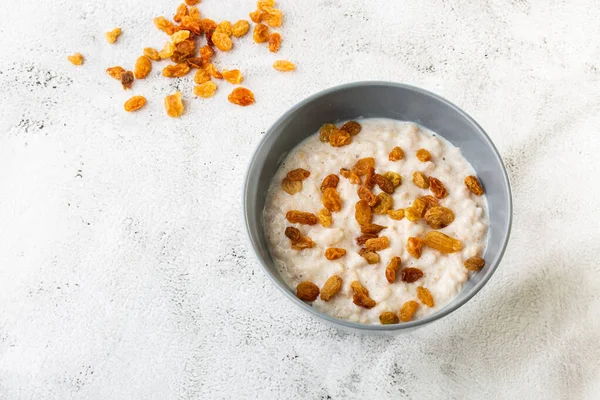 Oatmeal porridge or porridge oats or breakfast cereals with raisins isolated on white marble background. Homemade food. Tasty breakfast. Selective focus. Horizontal photo.