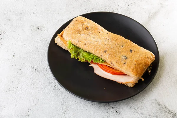 Baguette sandwich with salami, turkey breast, cheese, lettuce, tomatoes and onion on a cutting board. Long subway sandwiches isolated on white marble background. Homemade food. Tasty breakfast. Select