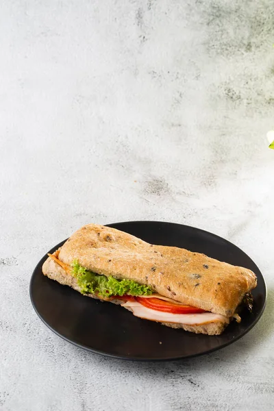 Baguette sandwich with salami, turkey breast, cheese, lettuce, tomatoes and onion on a cutting board. Long subway sandwiches isolated on white marble background. Homemade food. Tasty breakfast. Select