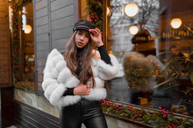 Doğal kısa beyaz kürk giyen güzel beyaz kadın Noel vitrininin yanındaki bir portre için poz veriyor. Noel dekoru. Moda. Tarz. Doğal kürkten yapılmış kışlık giysiler. Yatay.
