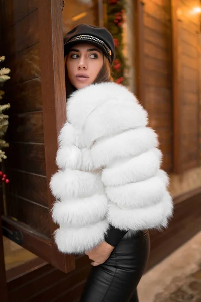 Bella giovane donna caucasica che indossa pelliccia bianca corta naturale in posa per un ritratto vicino alla vetrina di Natale. Arredo natalizio. Moda. Stile. Vestiti invernali in pelliccia naturale. Verticale — Foto Stock