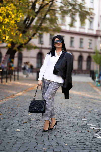 Autunno moda outdoor. La ragazza in elegante camicia bianca alla moda, pantaloni, giacca e occhiali da sole, stile di vita autunnale sullo sfondo di alberi sfocati giallo-verdi nel parco. Verticale — Foto Stock