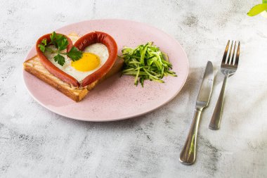 Kalp şeklinde çırpılmış yumurtalar, beyaz bir tabakta sosisli, ekşi ekmek, beyaz mermer arka planda izole edilmiş. Ev yapımı yemek. Lezzetli bir kahvaltı. Seçici odaklanma. Hotizontal fotoğraf.