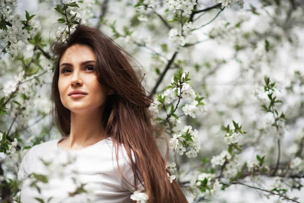 Fille debout sous le pommier en fleurs dans le parc naturel. Concept de mode. Elégante jeune femme en jeans vêtements appréciant jardin fleuri au jour ensoleillé du printemps.Maquillage beauté naturelle. Horizontal — Photo