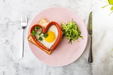Kalp şeklinde çırpılmış yumurtalar, beyaz bir tabakta sosisli, ekşi ekmek, beyaz mermer arka planda izole edilmiş. Ev yapımı yemek. Lezzetli bir kahvaltı. Seçici odaklanma. Hotizontal fotoğraf.