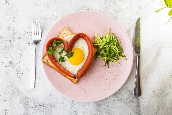 Kalp şeklinde çırpılmış yumurtalar, beyaz bir tabakta sosisli, ekşi ekmek, beyaz mermer arka planda izole edilmiş. Ev yapımı yemek. Lezzetli bir kahvaltı. Seçici odaklanma. Hotizontal fotoğraf.