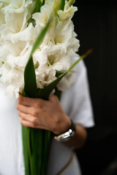 Mujer joven con ropa blanca sosteniendo ramo. Floristería Ramillete de flores. Florista. Arreglo con flores de gladiolo blanco. El concepto de una floristería. Florista de trabajo. espacio de copia —  Fotos de Stock