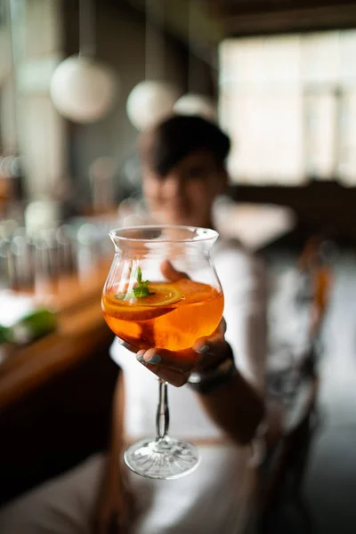 Vacker kvinna med kort brunett hår i vita kläder. Mode gatufotografering. Mode modell poserar med aperol cocktail på trä bakgrund. — Stockfoto