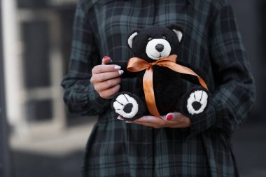 Oyuncak ayıyı tutan kadın eller. Kadın oyuncak ayıyı göstererek teslim oldu. Güzel bir Noel hediyesi. Kış tatili konsepti. Elinde altın bir yay olan oyuncak ayı. Gri arka planda. Yatay