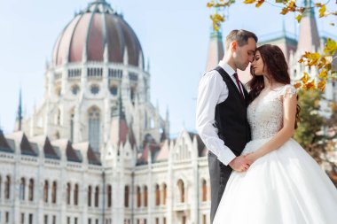 Gelin ve damat eski kasaba caddesinde sarılıyor. Düğün çifti Budapeşte 'de Parlamento Binası yakınlarında yürüyor. Kafkasyalı mutlu romantik çift evliliklerini kutluyor. Düğün ve aşk konsepti.