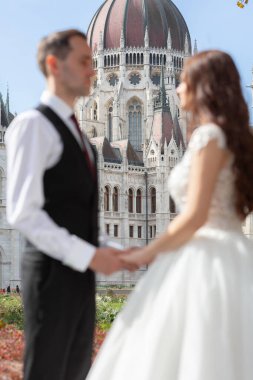 Gelin ve damat eski kasaba caddesinde sarılıyor. Düğün çifti Budapeşte 'de Parlamento Binası yakınlarında yürüyor. Kafkasyalı mutlu romantik çift evliliklerini kutluyor. Düğün ve aşk konsepti.