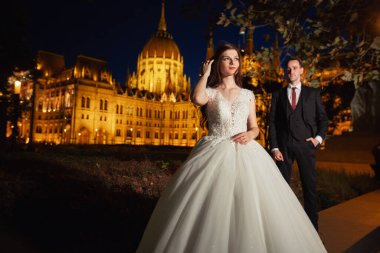 Gelin ve damat eski kasaba caddesinde sarılıyor. Düğün çifti Budapeşte 'de Parlamento Binası yakınlarında gece yürüyüşe çıkıyor. Evliliklerini kutlayan mutlu romantik genç çift. Düğün ve aşk konsepti.