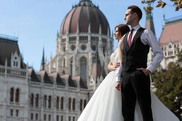 Gelin ve damat eski kasaba caddesinde sarılıyor. Düğün çifti Budapeşte 'de Parlamento Binası yakınlarında yürüyor. Kafkasyalı mutlu romantik çift evliliklerini kutluyor. Düğün ve aşk konsepti.