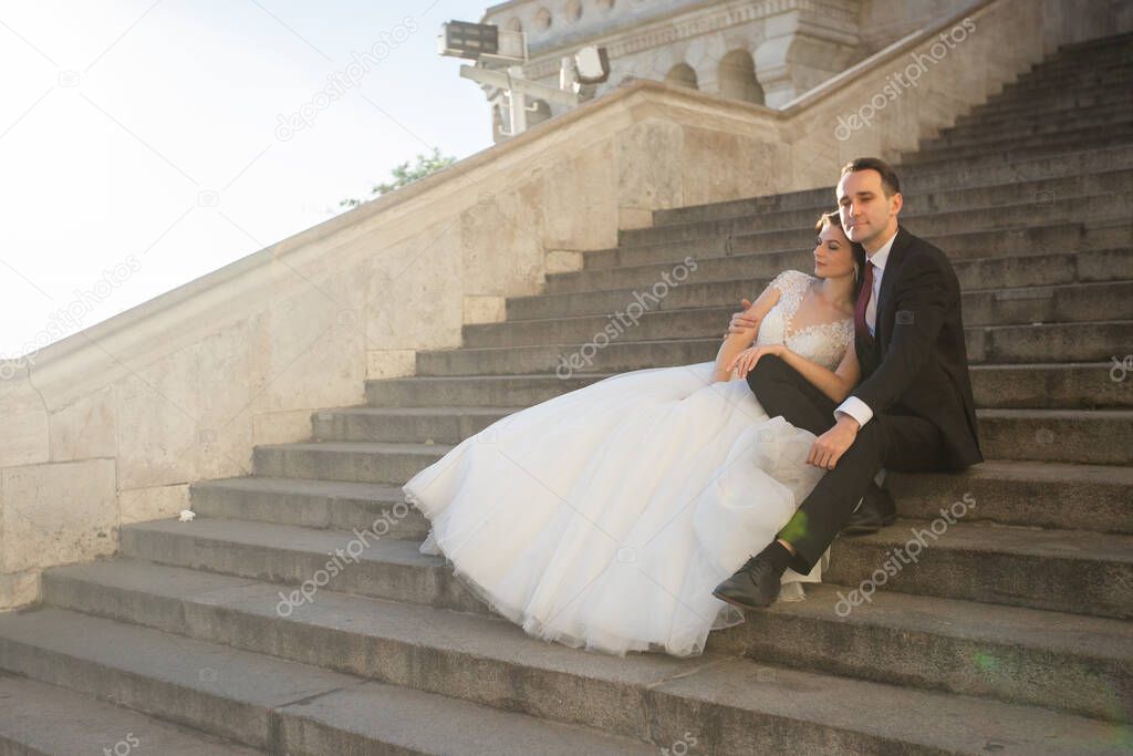 Bride and groom hugging in the old town street. Wedding couple sit on the Fishermans Bastion, Budapest, Hungary. Happy romantic young couple celebrating their marriage. Wedding and love concept.