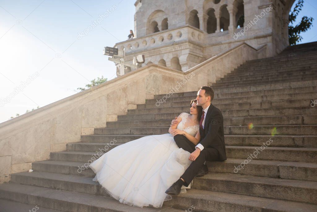 Bride and groom hugging in the old town street. Wedding couple sit on the Fishermans Bastion, Budapest, Hungary. Happy romantic young couple celebrating their marriage. Wedding and love concept.