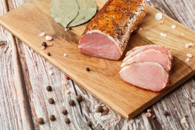 Kesme tahtasında tütsülenmiş jambon. Ahşap bir masada dilimlenmiş tütsülenmiş tavla.