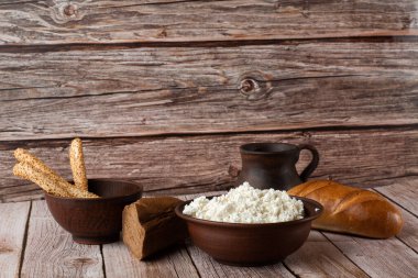 Tahta bir kâse içinde taze süzme peynir ve bir kaşık, ahşap arka planda bir kavanoz ekşi krema. Protein ve kalsiyum açısından zengin sağlıklı süt ürünü, düşük yağlı yumuşak beyaz peynir.