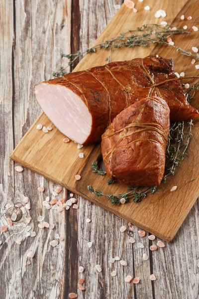 Smoked ham on a chopping board. Sliced smoked gammon on a wooden table with addition of fresh herbs and aromatic spices.