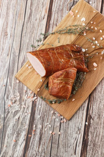 Smoked ham on a chopping board. Sliced smoked gammon on a wooden table with addition of fresh herbs and aromatic spices.