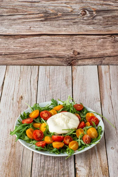 Lezzetli, mozzarella burrata, roka, kiraz domatesleri ve ahşap bir arka planda beyaz bir tabakta fesleğen. Yaklaş. Sağlıklı İtalyan yemekleri