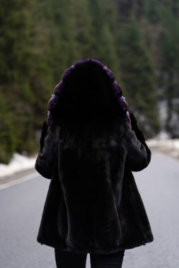 Kışlık orman arka planında poz veren bir kız. Şık bir süveter, mor moda kürk manto giyen alımlı, komik, genç bir kadın. Kürk ve moda konsepti. Güzel insanlar..