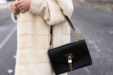 Şık bir kıyafet. Koyu renkli büyük siyah çantaya yaklaş. Sokakta poz veren, beyaz moda kürk giyen bir manken. Kürk ve moda konsepti. Güzel insanlar. Kadın moda konsepti.