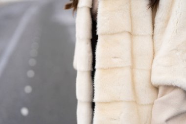 Kışın ormanlık alanda poz veren bir kız. Şık bir süveter giyen, beyaz moda kürk giyen çekici bir kadın. Kürk ve moda konsepti. Güzel insanlar..