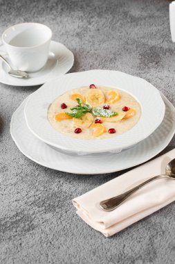 Beyaz kasede dilimlenmiş muzlu Semolina lapası ya da kahvaltı yulafı gri taş arka planda izole edilmiş. Ev yapımı yemek. Lezzetli bir kahvaltı. Seçici odaklanma. Dikey fotoğraf. Bardak ve çaydanlık..